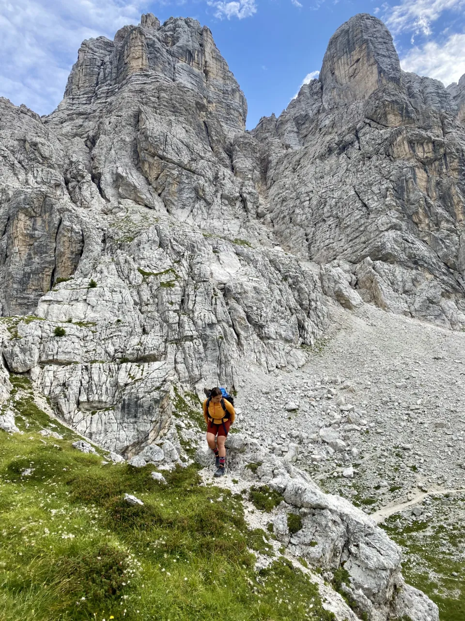 Hiker climbing a rocky path beneath the towers of the Civetta group