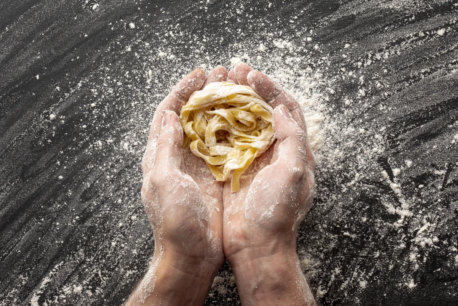 Hands holding a nest of fresh handmade tagliatelle dusted with flour