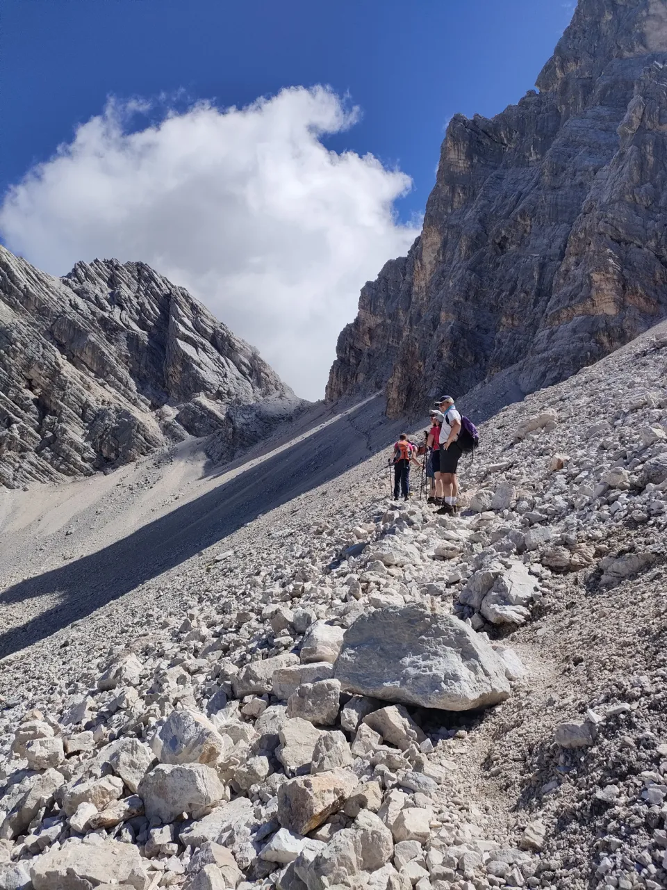 Group of hikers crossing a scree slope beneath towering Dolomite walls
