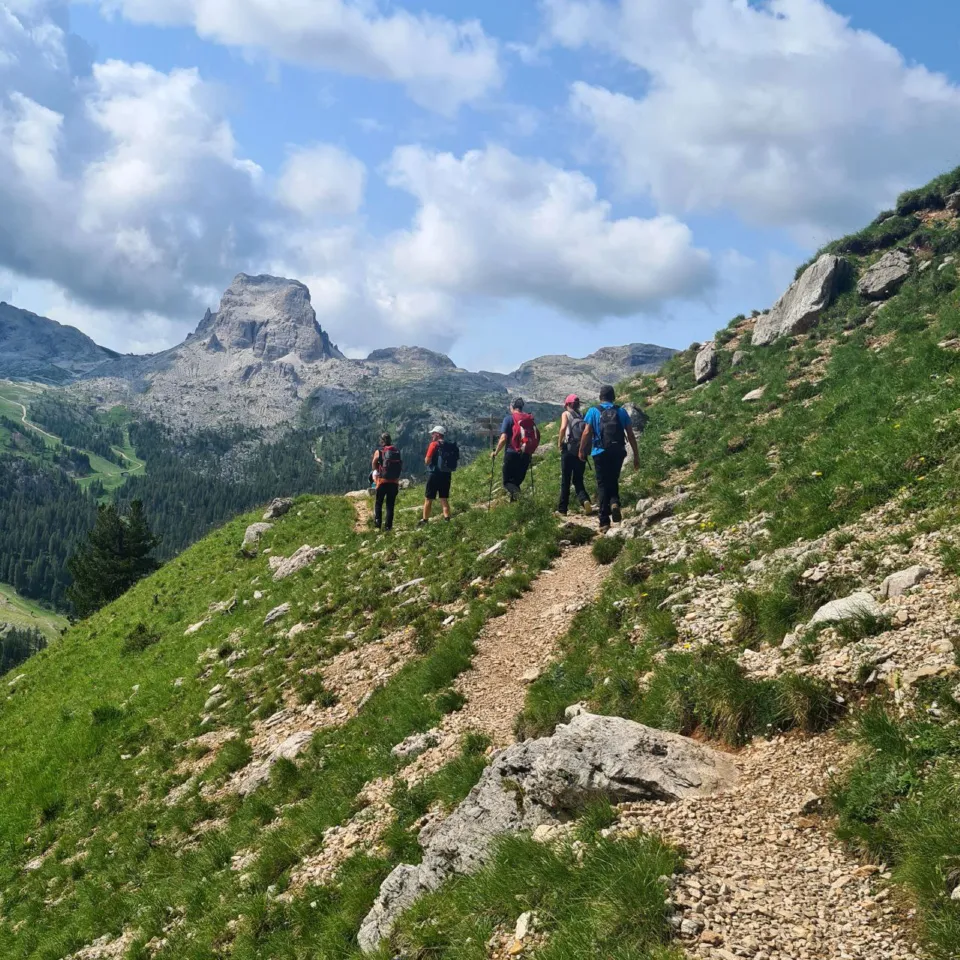 Hikers walking a grassy mountain trail towards a Dolomite peak