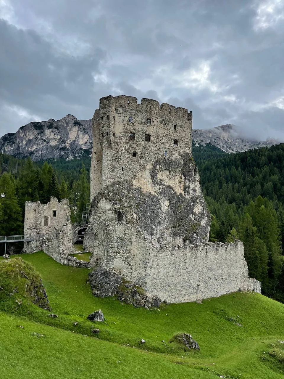 Ruins of Andraz Castle on a green meadow beneath the Dolomites